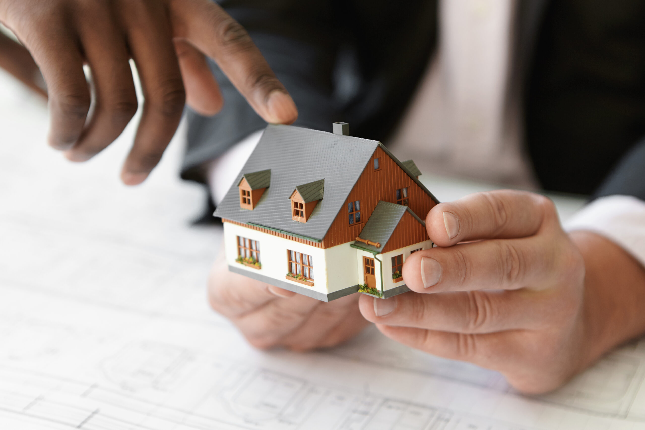 500sqm or 300sqm: Which Plot Size Is Right for You? close up shot of caucasian contractor holding real estate project while his african colleague pointing finger at scale model building, explaining design during presentation meeting in office