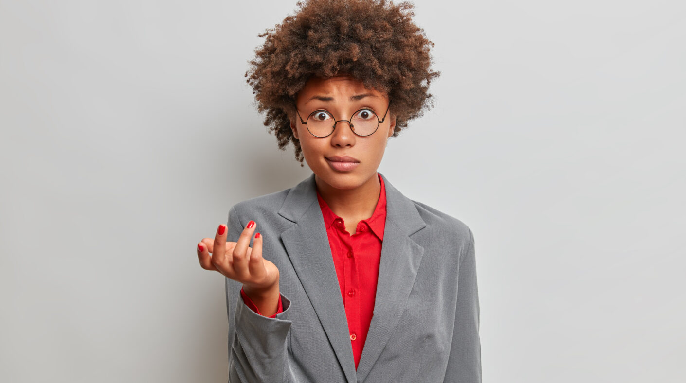 Before You Buy Any Land, Ask These 7 Questions confused puzzled female director, owner of business company, shrugs shoulders with puzzlement, dressed formally, wears round glasses, stands against grey studio background, has no idea what happening